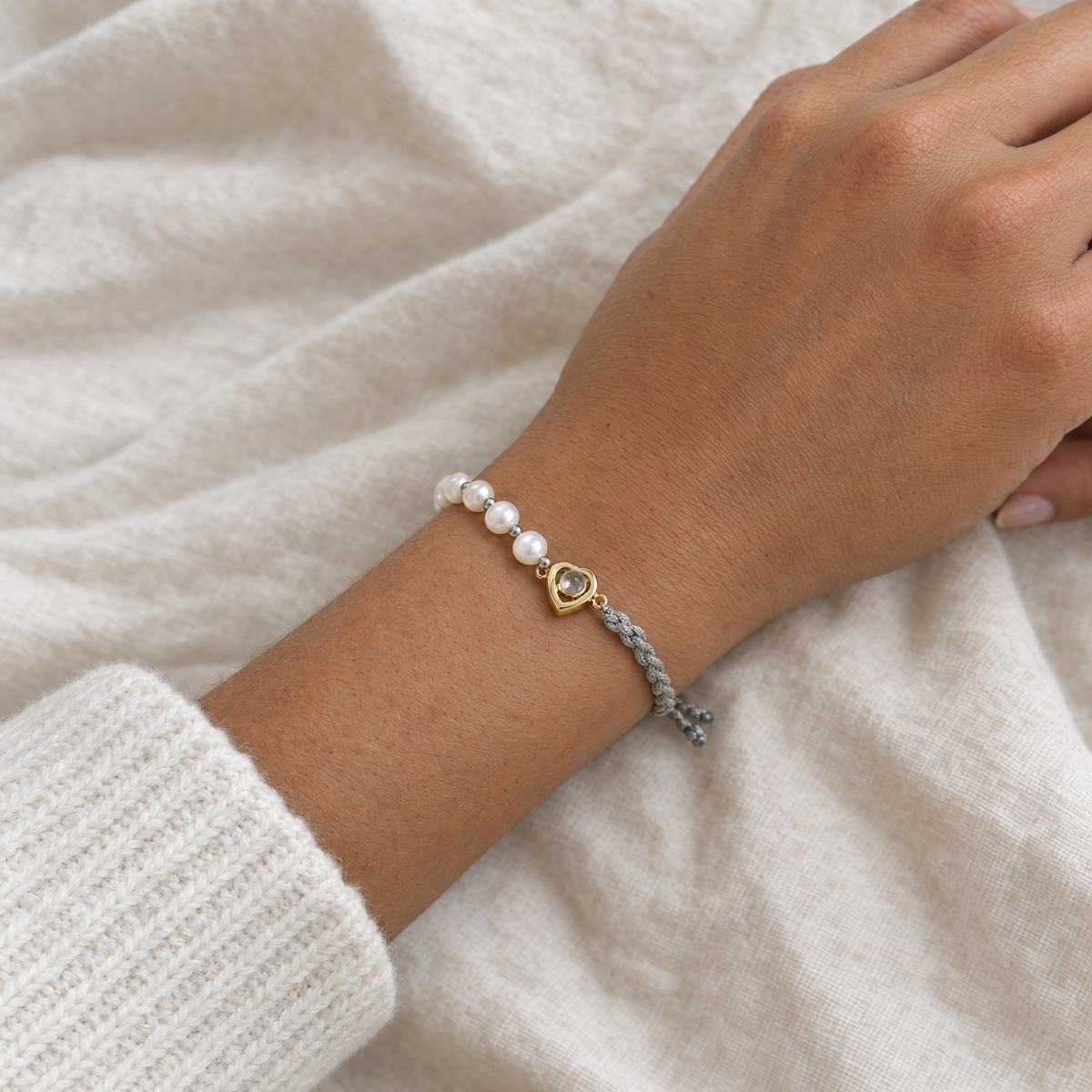 Muñeca con la pulsera de perlas y cordón gris con el corazón dorado